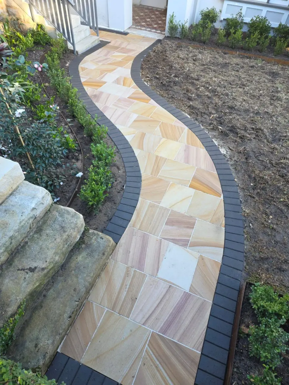 Close view of sandstone paving and dark brick borders
